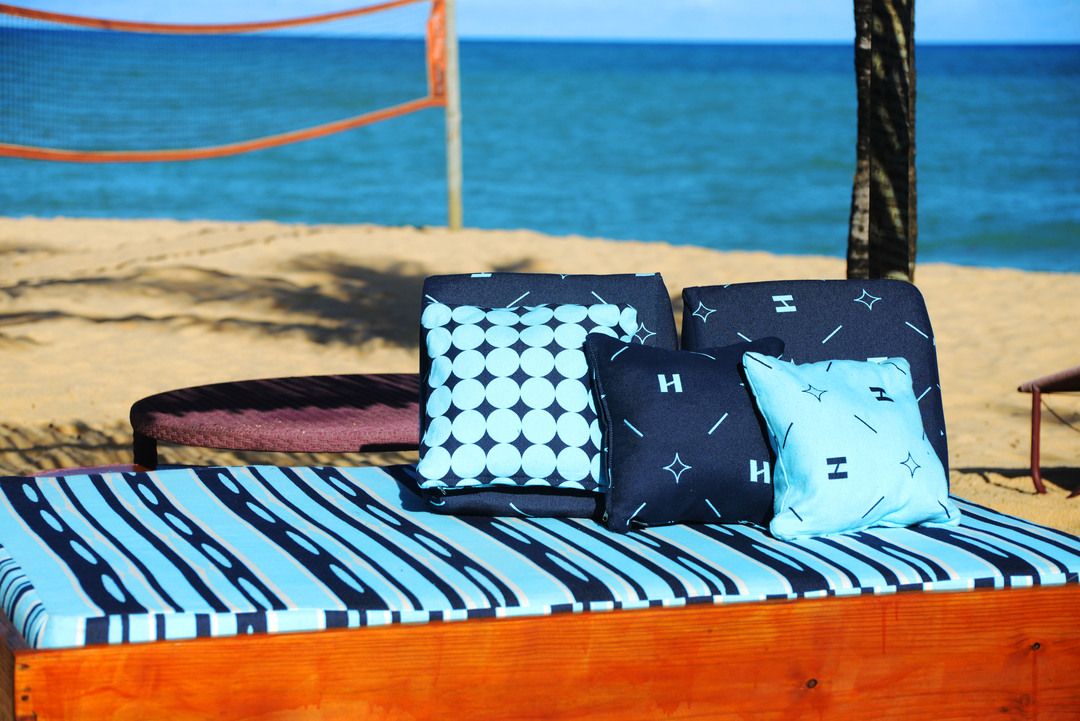 Um sofá com vista para a praia de Trancoso e uma rede de vôlei na areia. 